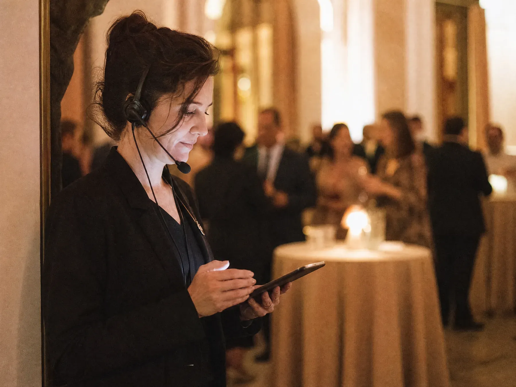 An event producer in a headset reviews incoming posts on a tablet at the side of a corporate event.