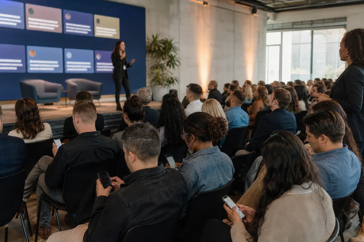 Employees contributing from their seats during a company town hall with a private live wall near the speaker.