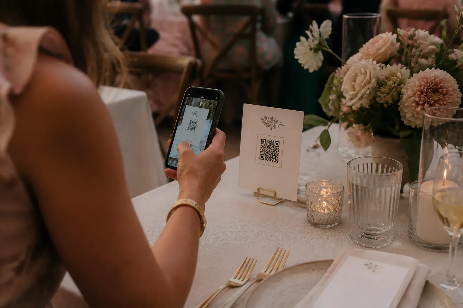 An elegant QR code guest book card on a wedding table as a guest scans it with a phone.