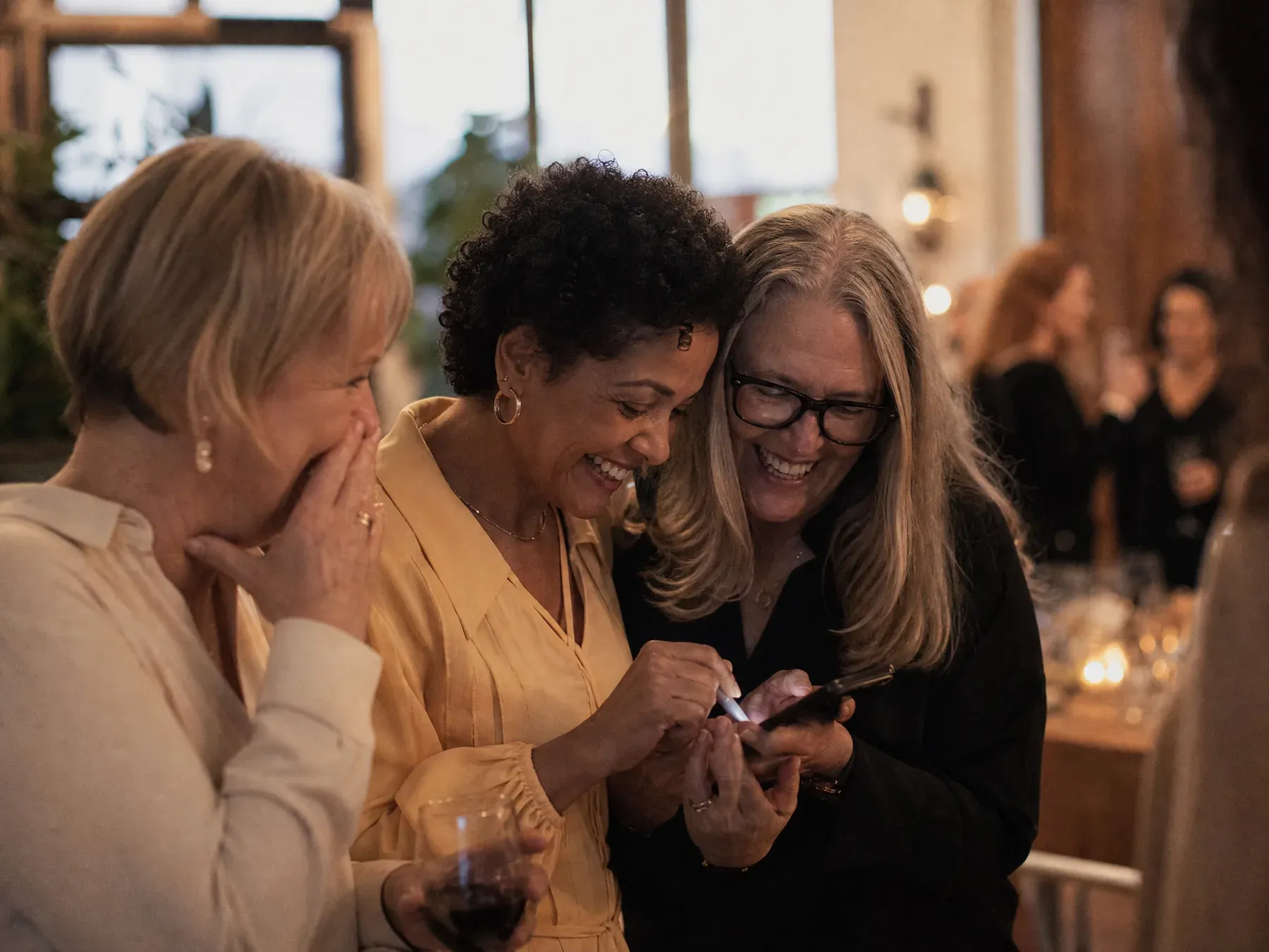 Three colleagues huddle over one phone writing a message together at a retirement party.